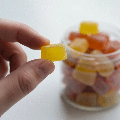 Close-up of a hand holding a single CBD gummy, blurred background of other gummies in a jar, emphasizing individual use
